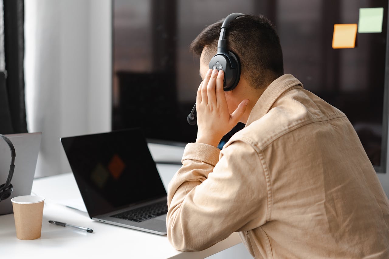 Services-02 A man wearing headphones works at a laptop in a modern office setting.